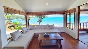 Ein Zimmer mit großem Fenster und Meerblick, Holzboden, einer Couch mit Kissen und einem kleinen Tisch.