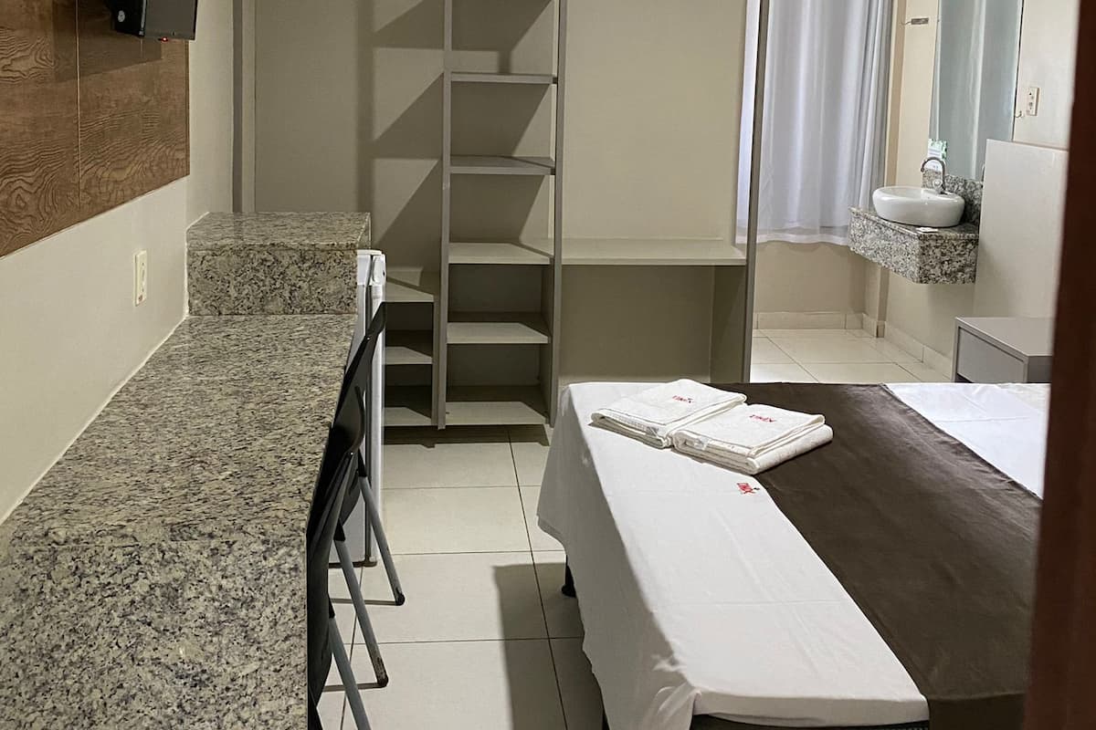 Habitación de hotel con cama, escritorio, silla, armario, baño con lavabo y espejo, y televisor montado en la pared.