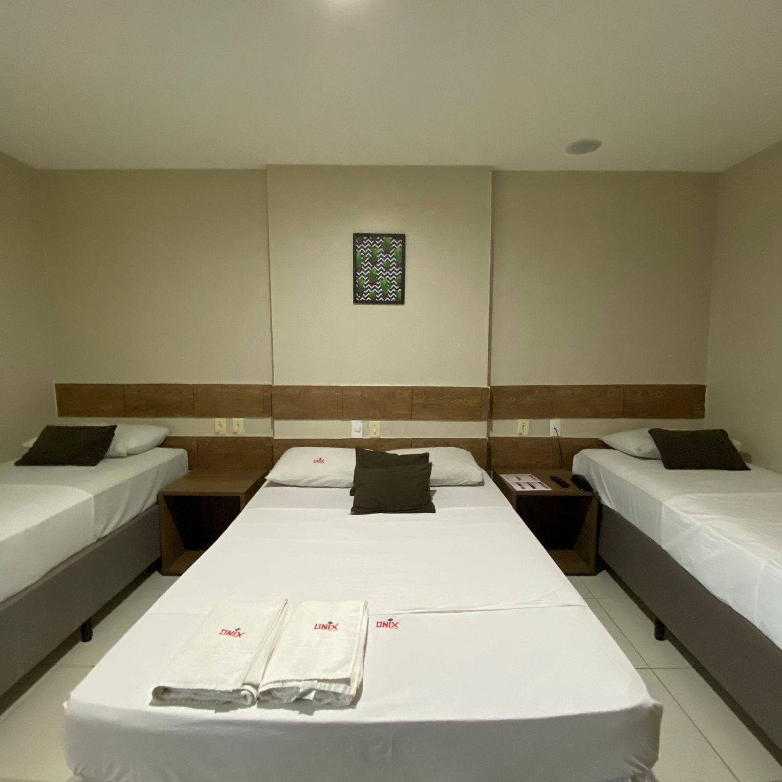 Quarto de hotel com duas camas de solteiro, uma cama de casal e uma mesa de cabeceira com um controle remoto.