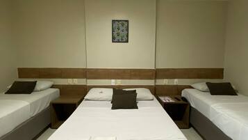 Quarto de hotel com duas camas de solteiro, uma cama de casal e uma mesa de cabeceira com um controle remoto.