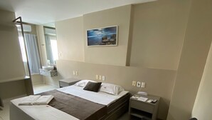 Habitación de hotel con cama, escritorio, silla, mesita de noche y ventana con cortinas.