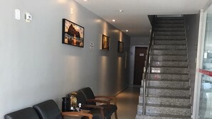 Zona de recepción con una escalera, un mostrador y tres sillones de cuero negro.