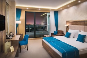 Une chambre d’hôtel moderne dotée d’un grand lit, d’un bureau, d’une chaise et d’un balcon offrant une vue sur la ville.
