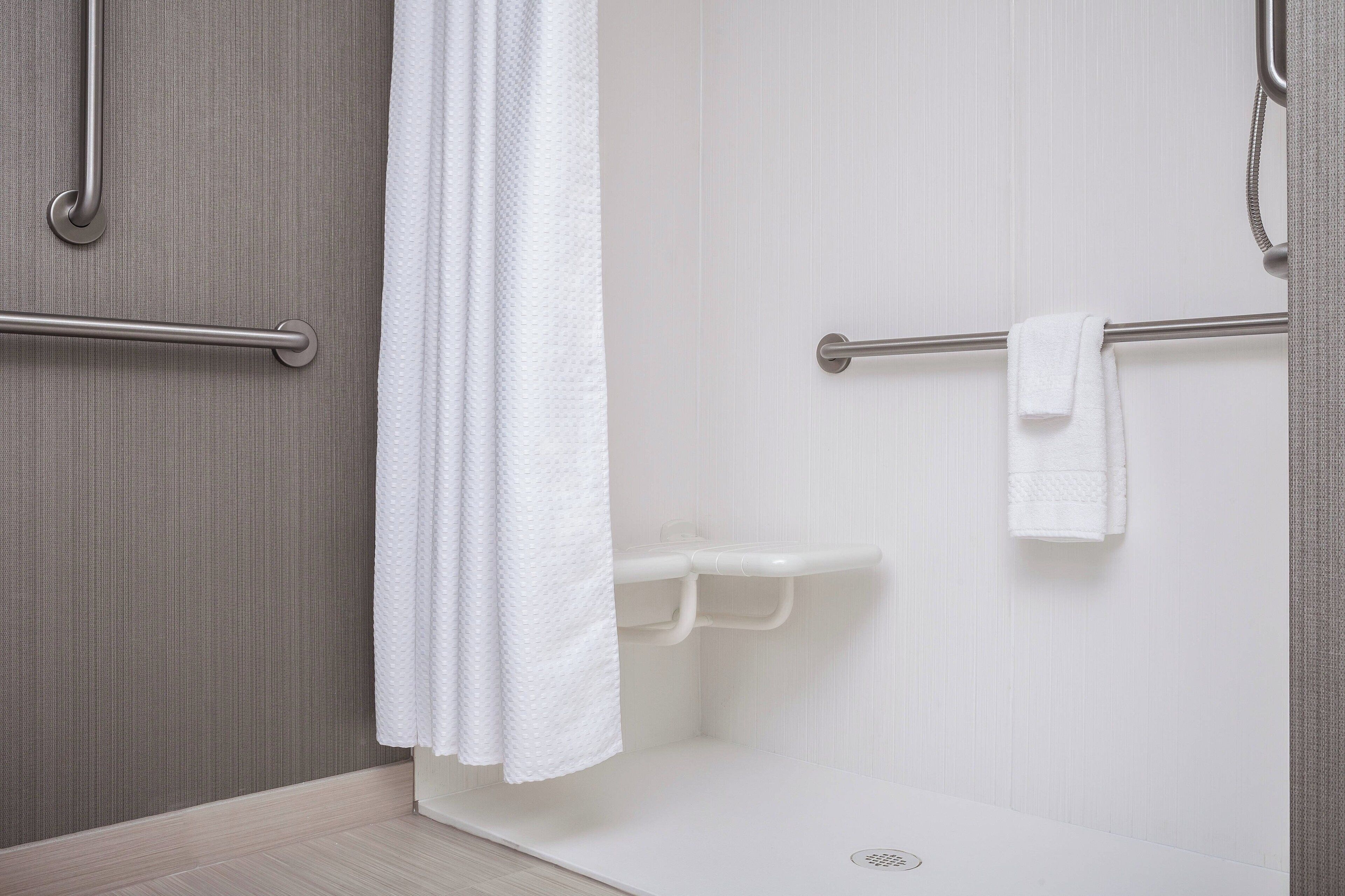 A modern bathroom with a shower, grab bars, and a white towel rack.