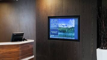A reception desk with a digital display showing local events and a mountainous landscape.