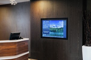 Una mesa de recepción con una pantalla digital que muestra eventos locales y un paisaje montañoso.
