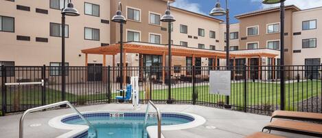 A hotel pool area with a hot tub, lounge chairs, and a covered seating area.