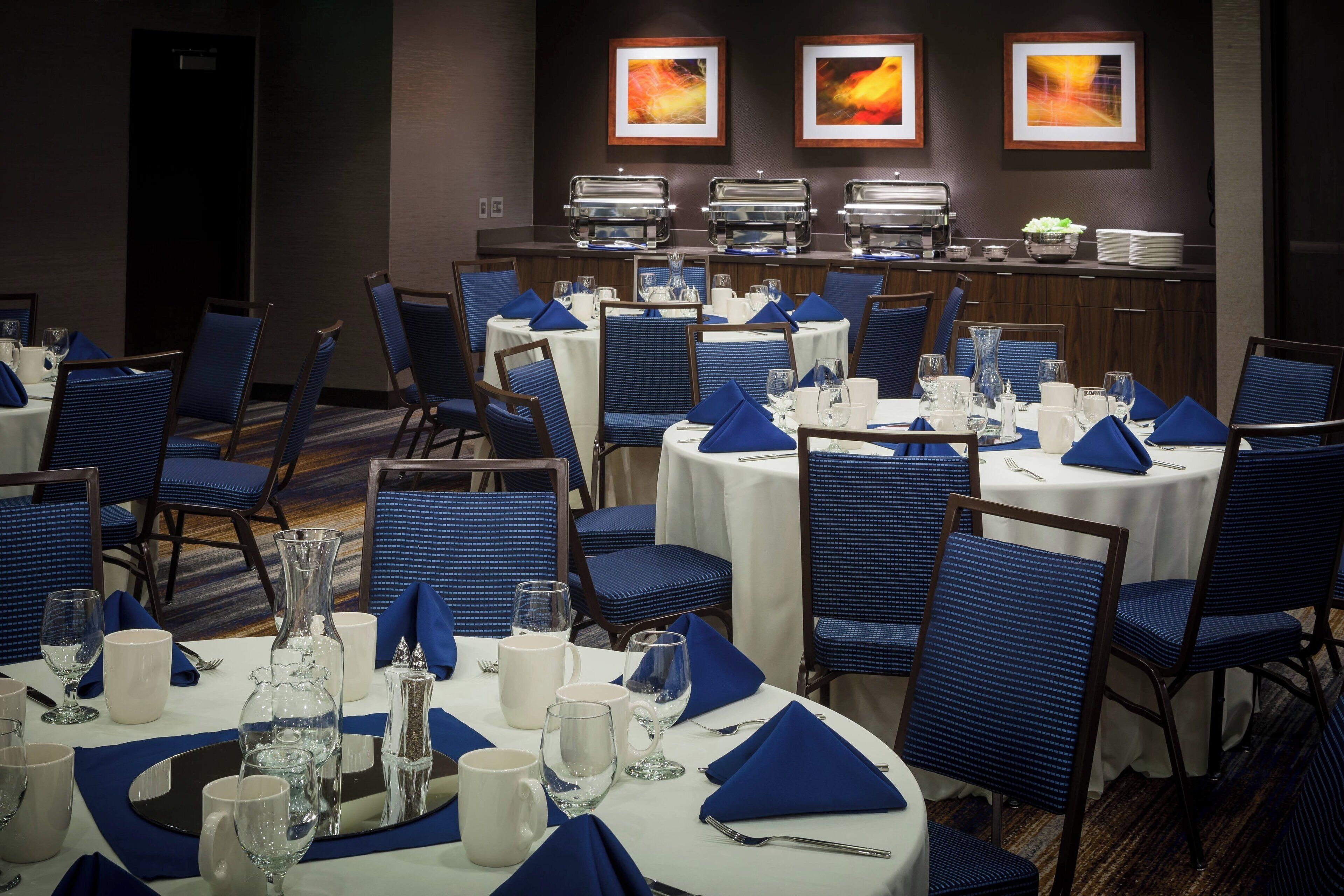 A dining area with round tables set for service, blue upholstered chairs, and buffet stations in the background.