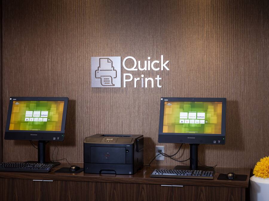 A print station with two monitors, a printer, and a keyboard on a wooden desk.