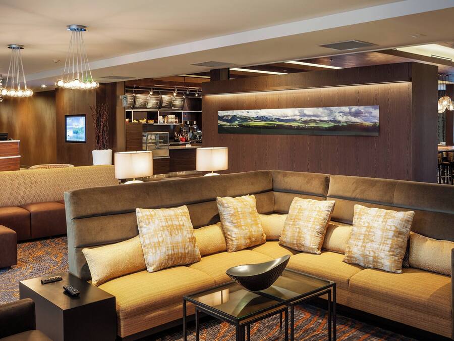A modern hotel lobby with a sectional sofa, a bar area, and a large landscape painting on the wall.