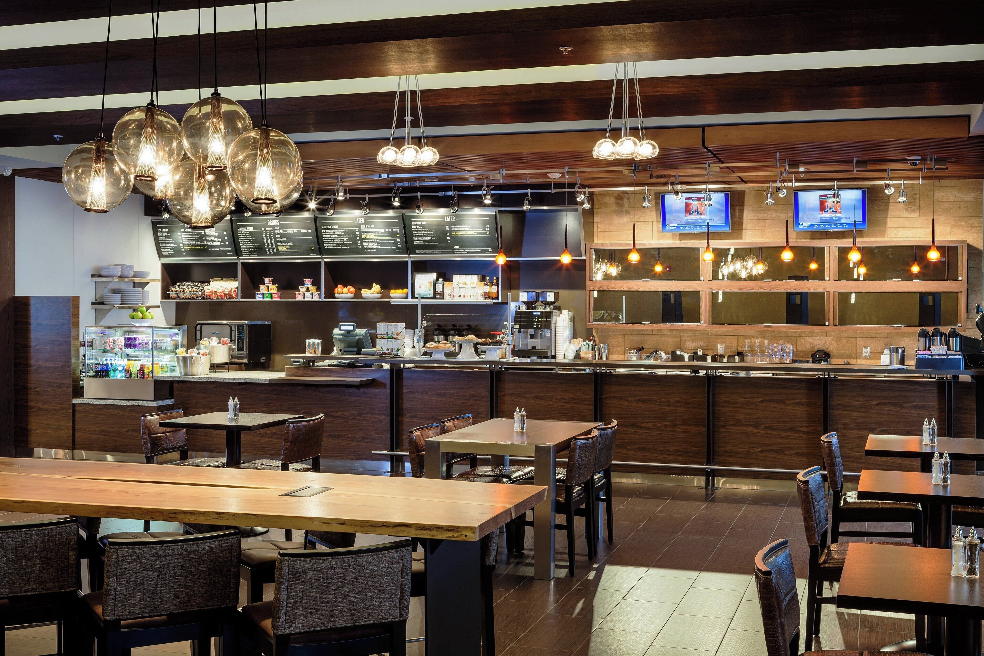 Un restaurant moderne avec des tables et des chaises en bois, un comptoir où est affiché le menu, et des lampes suspendues.