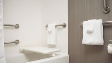 Un baño con una bañera blanca, una barra de apoyo y un perchero con dos toallas.
