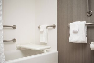 Un baño con una bañera blanca, una barra de apoyo y un perchero con dos toallas.