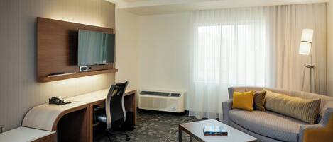 Une chambre d’hôtel équipée d’un bureau, d’une chaise, d’un canapé et d’un téléviseur à écran plat fixé au mur.