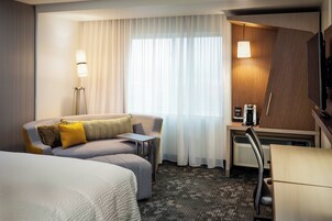 Una habitación de hotel con cama, sofá, escritorio, silla, lámpara y televisor.