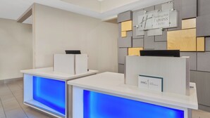 A reception area with a modern design, featuring a reception desk with a blue illuminated panel, a sign for Holiday Inn Express & Suites, and a wall with a geometric pattern.