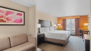 A hotel room with a bed, a sofa, a desk, and a window with curtains.