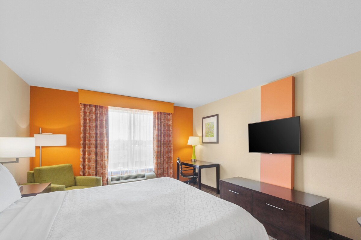 A hotel room with a large bed, a desk, a chair, a TV, and a window with curtains.