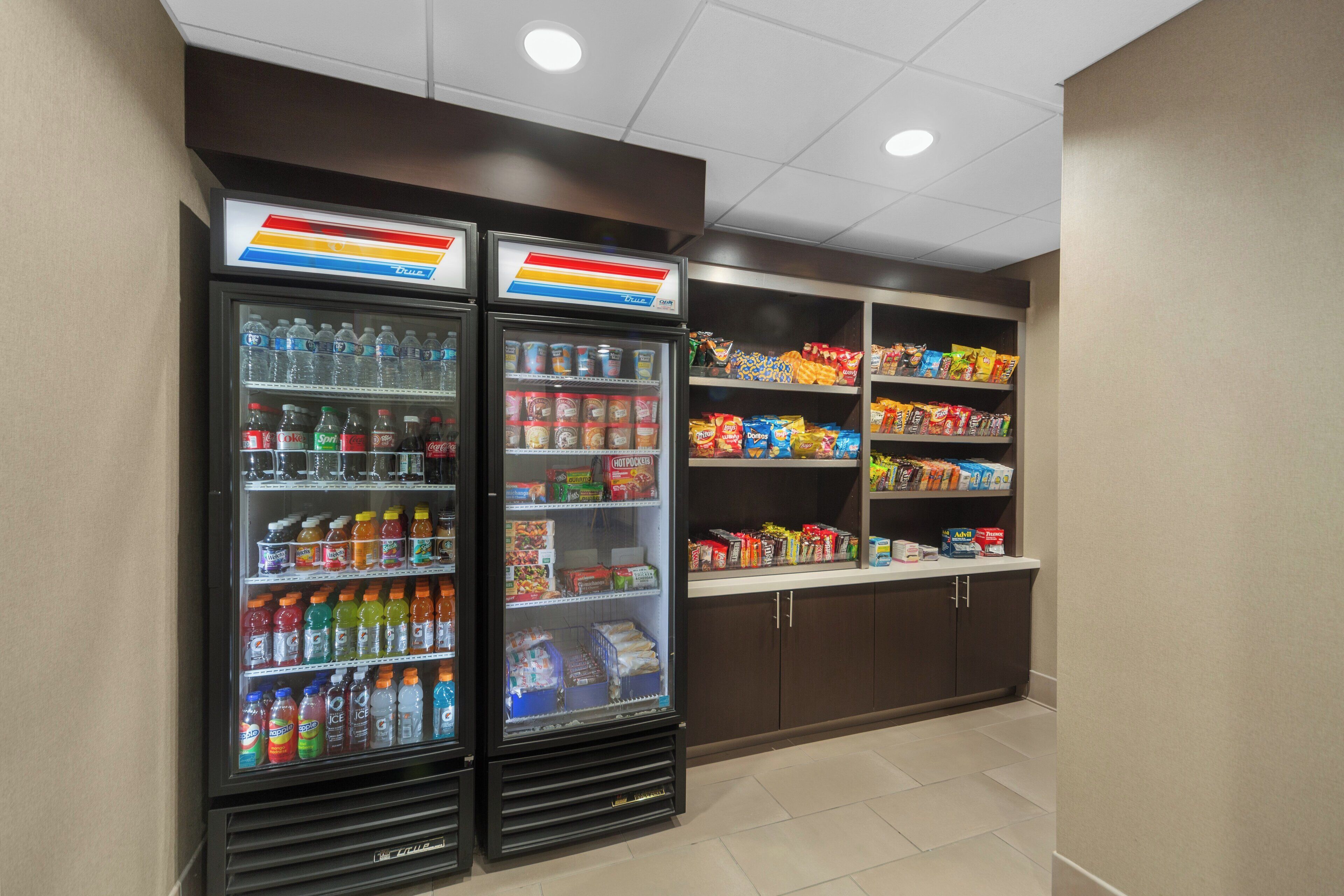 A vending area with two refrigerated beverage dispensers and shelves stocked with snacks and beverages.
