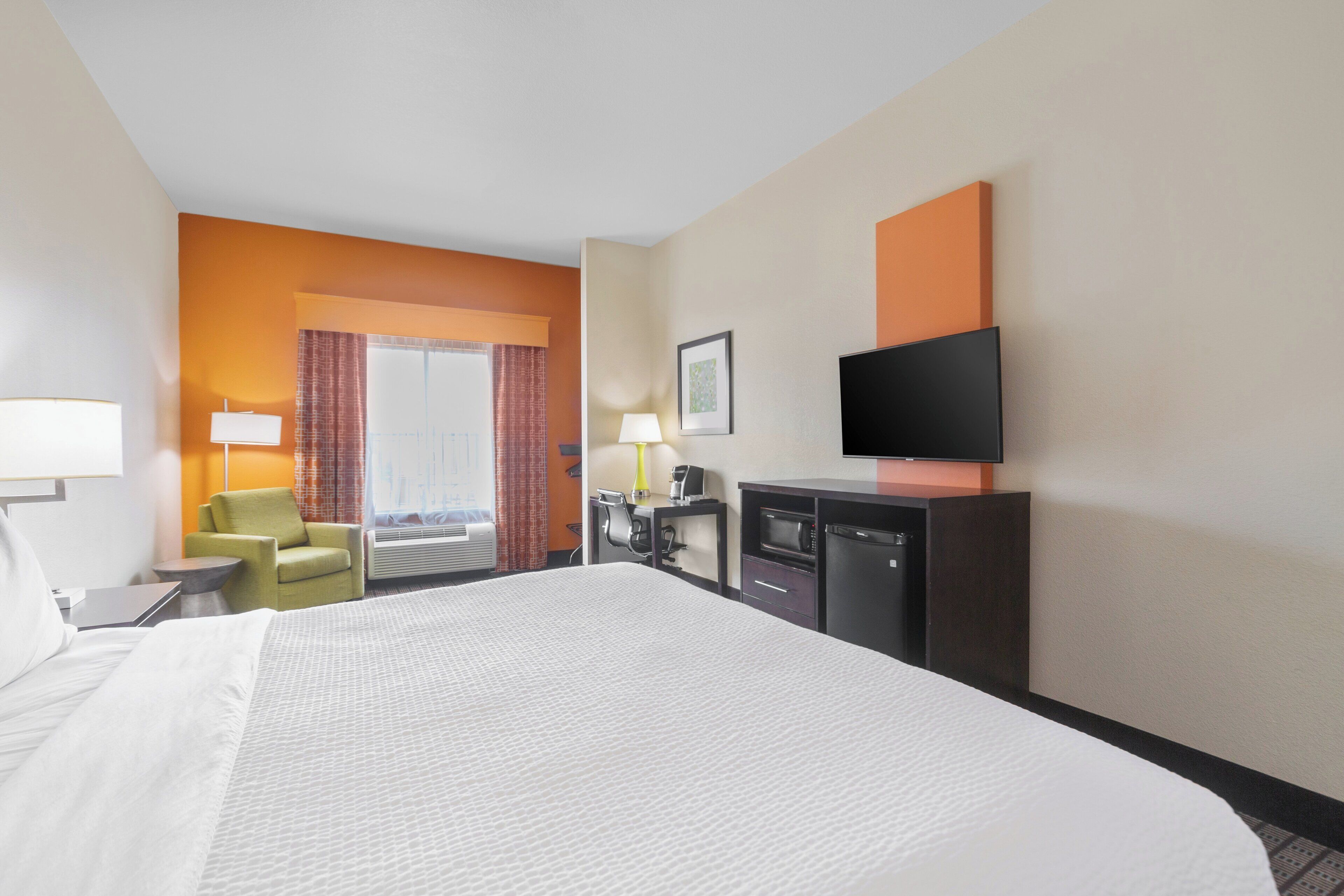 A hotel room with a large bed, a desk, a chair, a TV, and a window with curtains.
