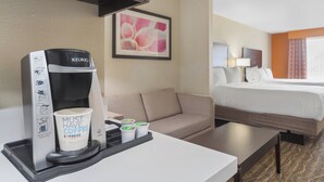 A hotel room with a coffee maker, a couch, a bed, and a framed picture on the wall.