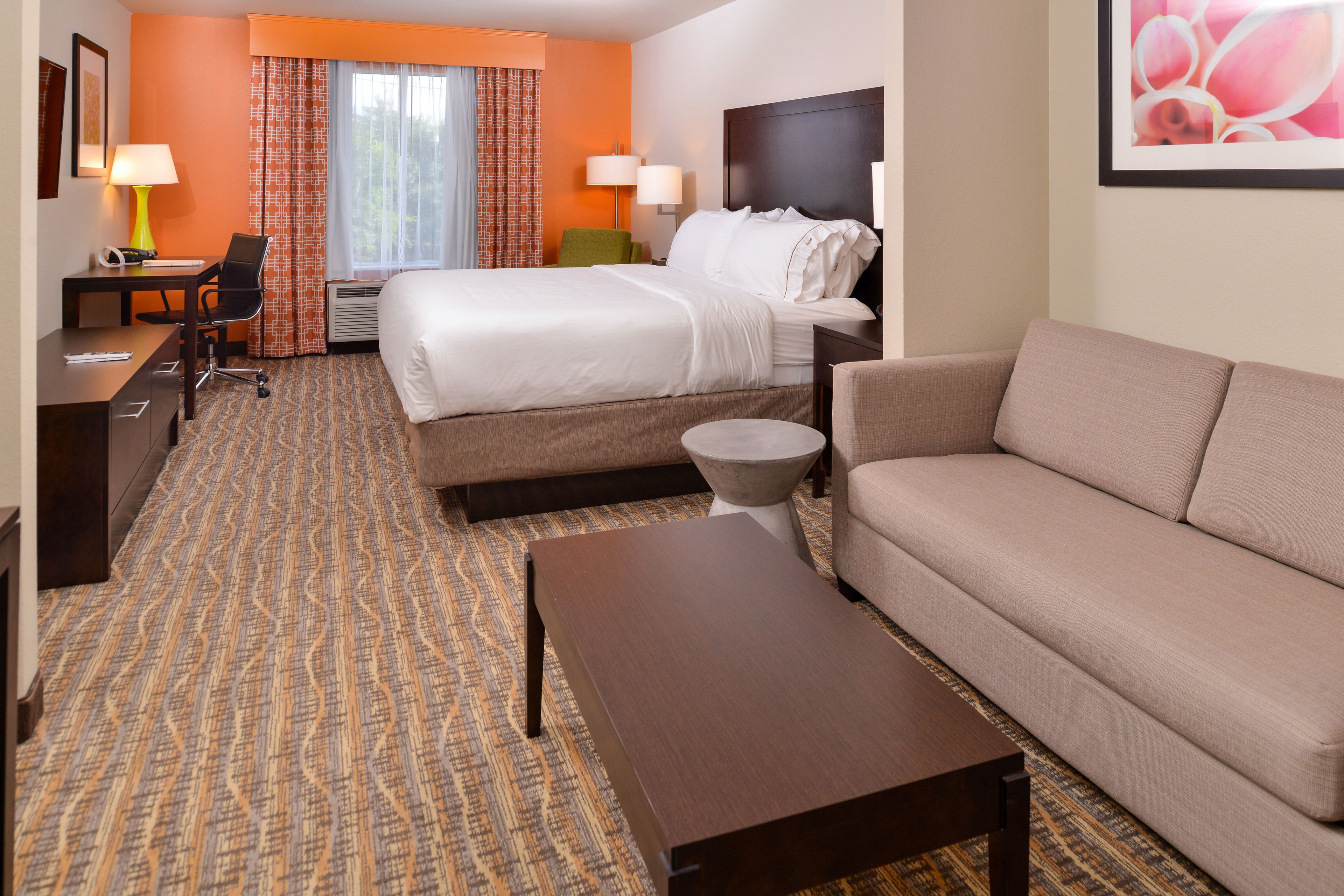 A hotel room with a bed, a sofa, a desk with a chair, a coffee table, and a lamp.