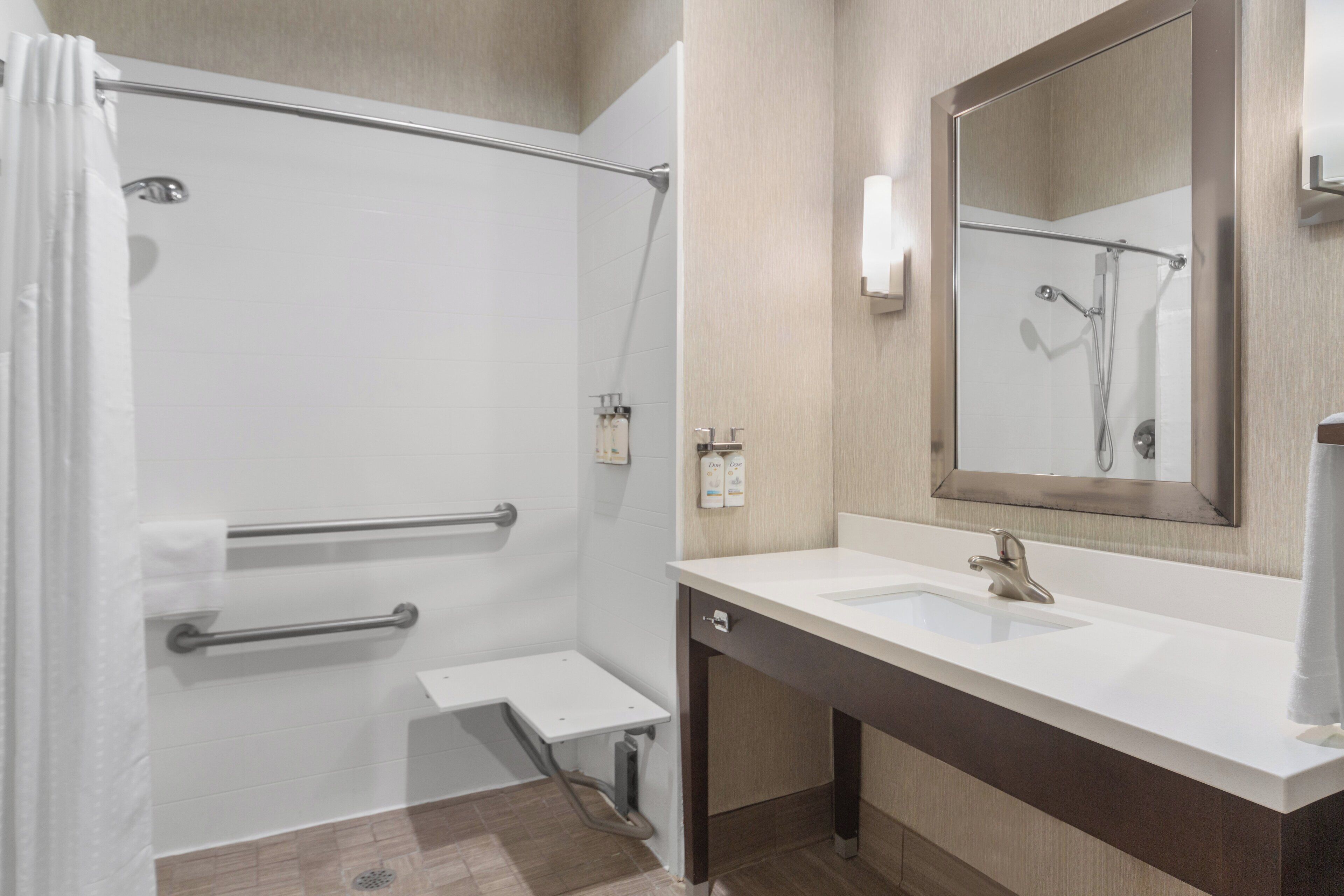 A modern bathroom with a walk-in shower, grab bars, a vanity with a sink, and a large mirror.