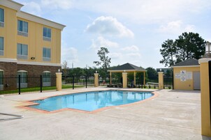 Zona de piscina con un edificio de ladrillo, un pabellón y una zona vallada.