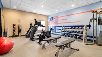Un gimnasio con equipo de ejercicio, una pared con texto motivacional y un soporte de mancuernas en la pared.