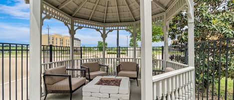 A gazebo with a hexagonal roof, outdoor seating with cushioned chairs, and a central fire pit.