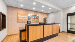 A reception desk with a 'Welcome to Hampton' sign, a wooden panel design, and a cityscape painting. - Hampton Inn Marion (Marion)