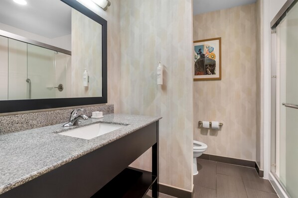 A modern bathroom with a granite countertop sink, a mirror, a toilet, and a shower area.