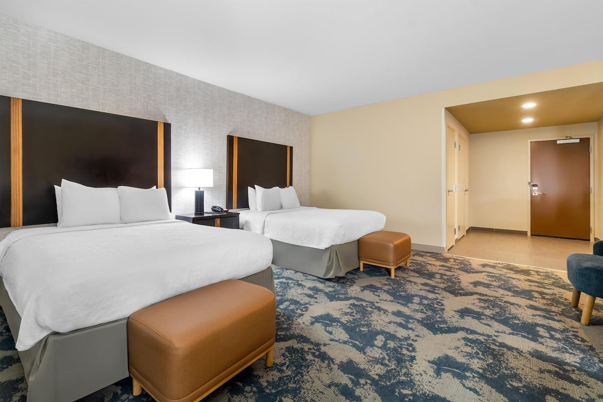 Habitación de hotel con dos camas, un escritorio, una silla y una puerta que da a otra habitación.