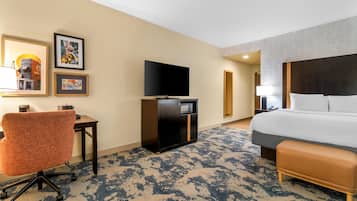 Habitación de hotel con cama, escritorio, silla, televisor y una obra de arte en la pared.