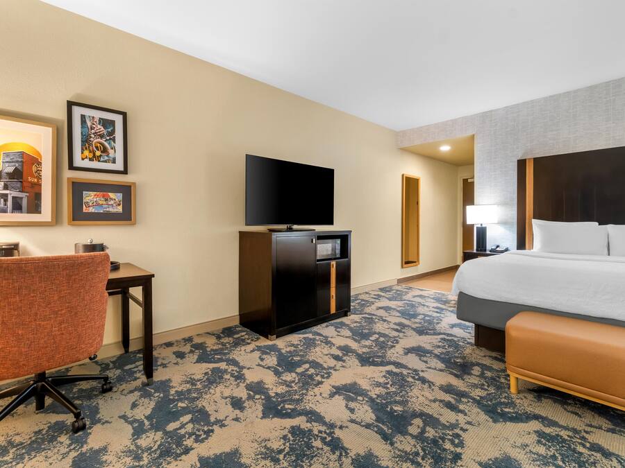 Habitación de hotel con cama, escritorio, silla, televisor y una obra de arte en la pared.
