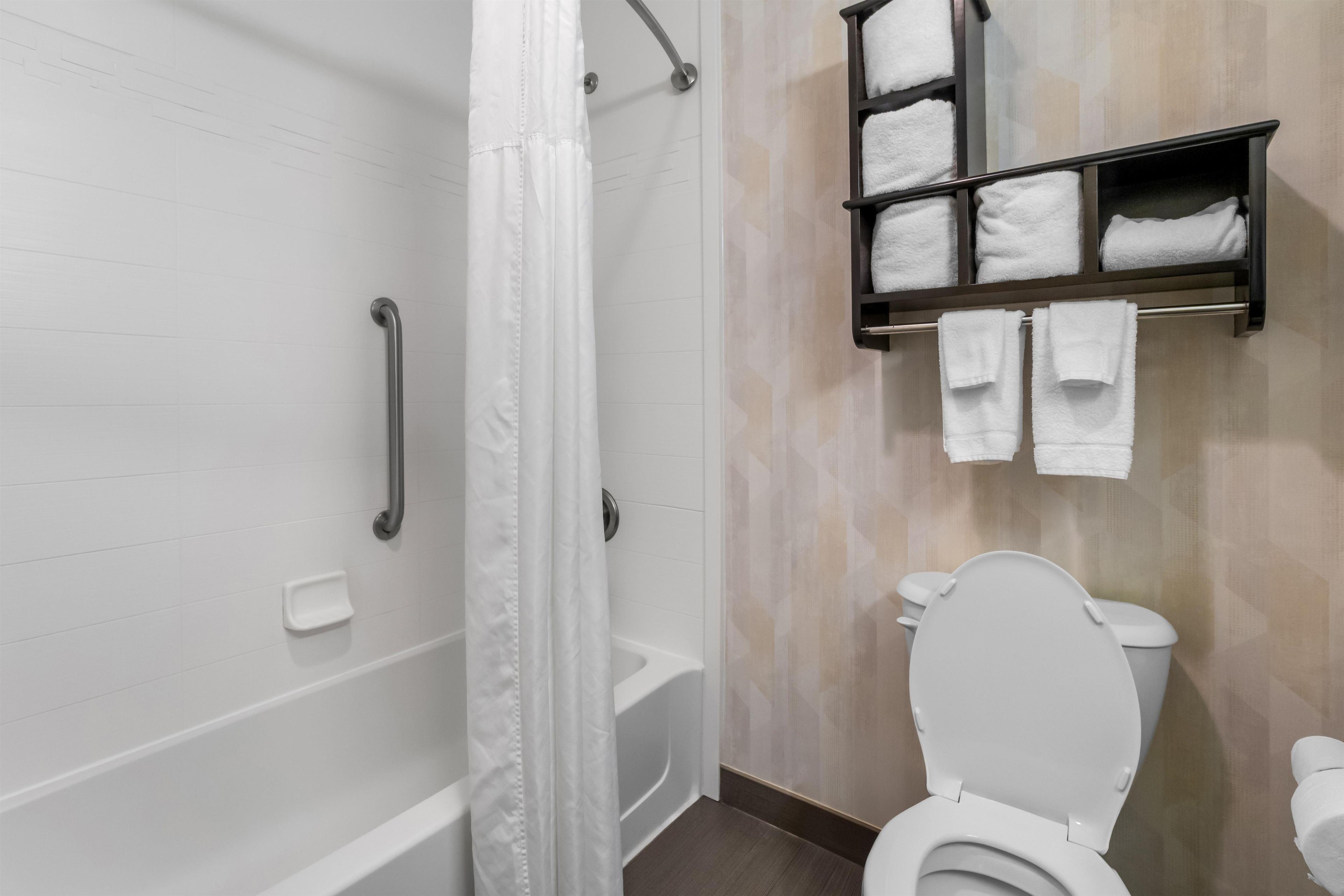 A bathroom with a white bathtub, a white toilet, a shower curtain, a grab bar, and a towel rack with towels.