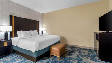 A hotel room with a bed, bedside lamps, a desk, a television, and a patterned carpet.