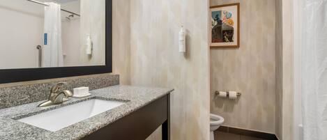 A bathroom with a granite countertop sink, a mirror, a toilet, and a shower curtain.