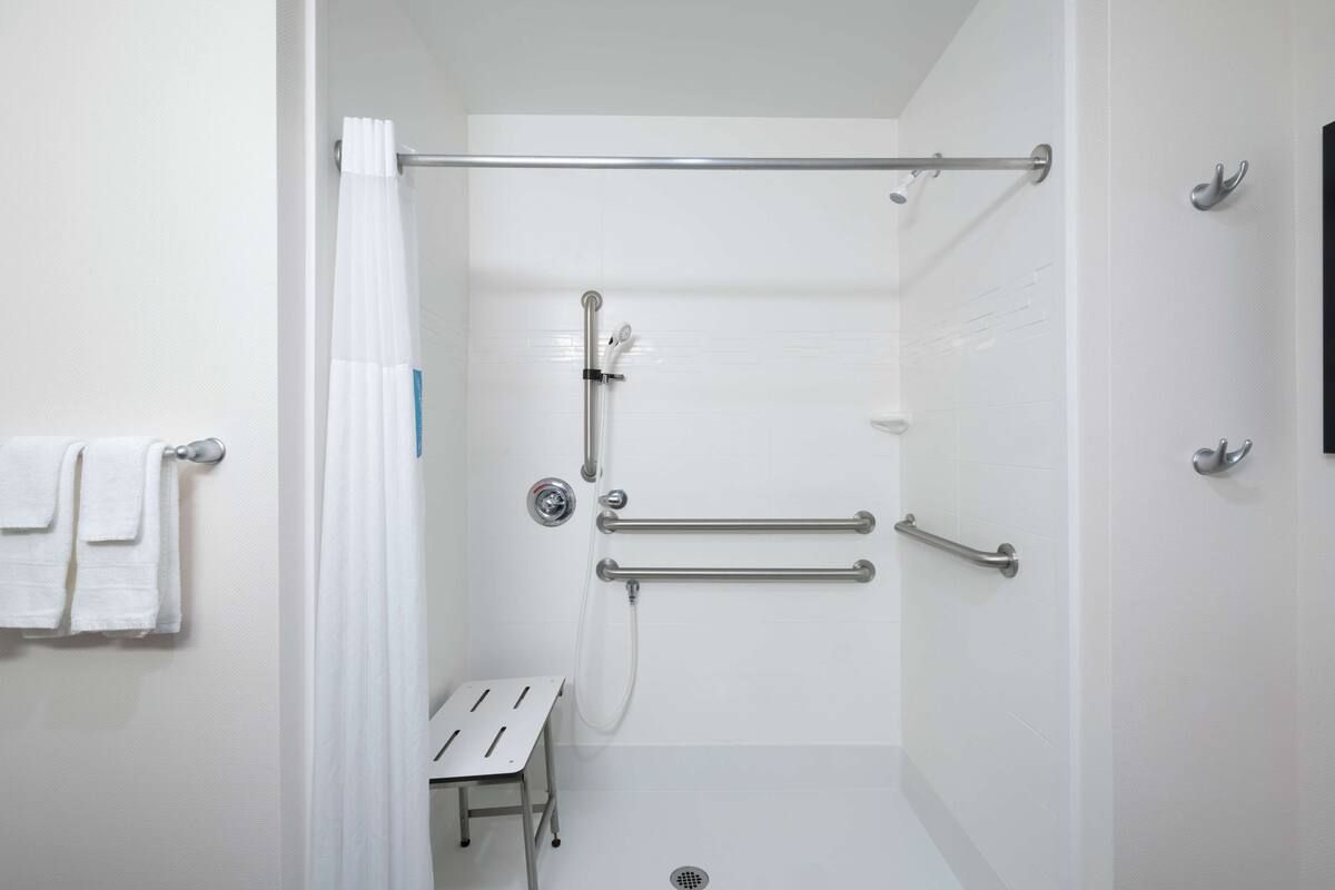Un baño moderno con azulejos blancos, ducha con puerta de cristal y barra de apoyo para mayor seguridad.