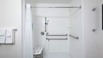 A modern bathroom with white tiles, a shower with a glass door, and a grab bar for safety.