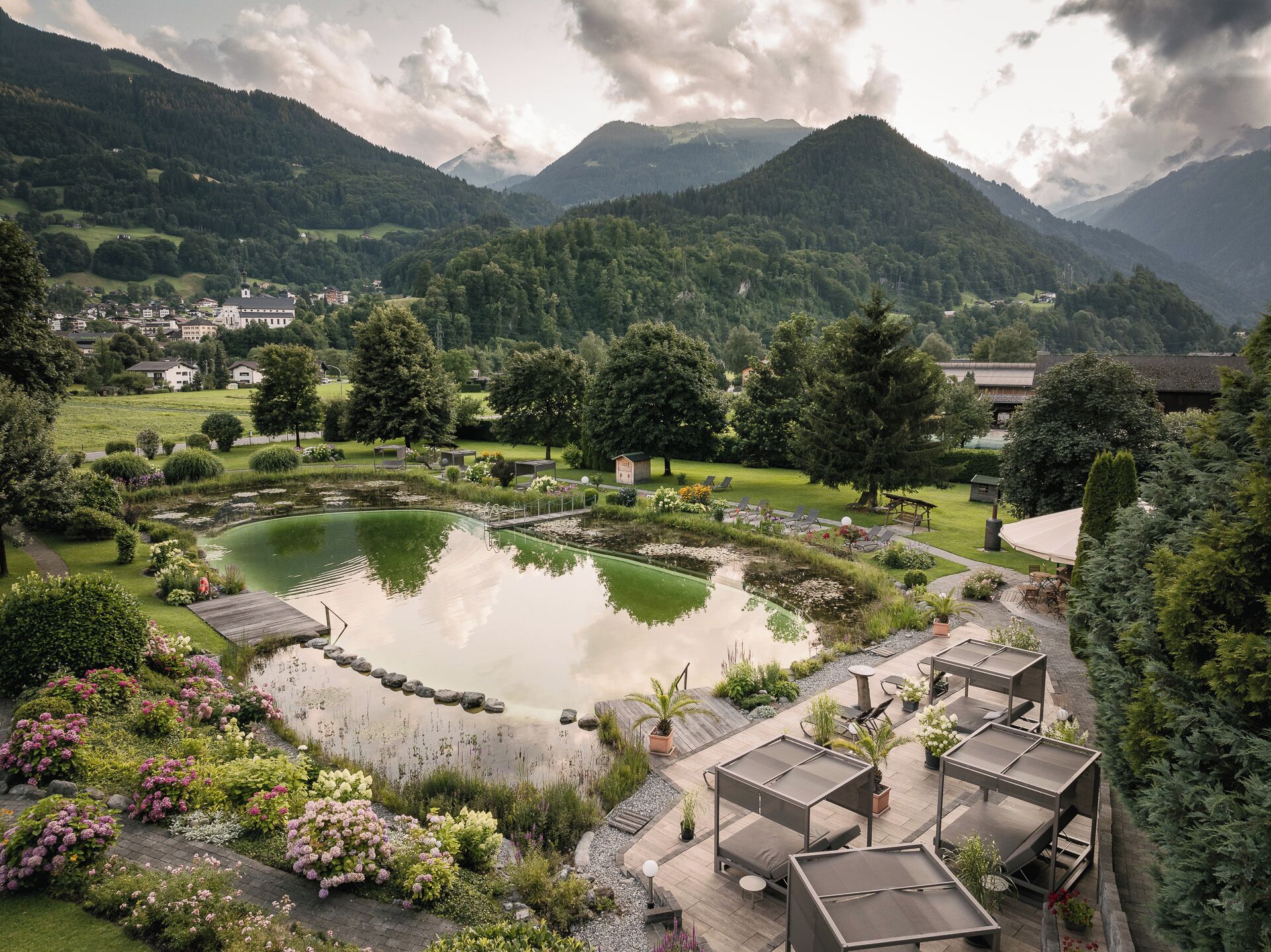 Un jardin d’hôtel paisible, avec un étang, des espaces de détente en plein air et une vue sur les montagnes.