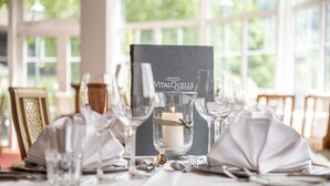 Een gedekte tafel voor een maaltijd, met een menukaartdoosje met de tekst 'VITALQUELLE MONTAFON' en een kaars als middelpunt.
