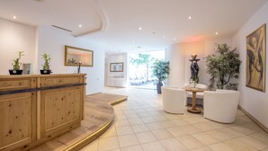 Een moderne hotelentree met een houten receptiebalie, witte zitplaatsen, potplanten en kunstwerken aan de muren.