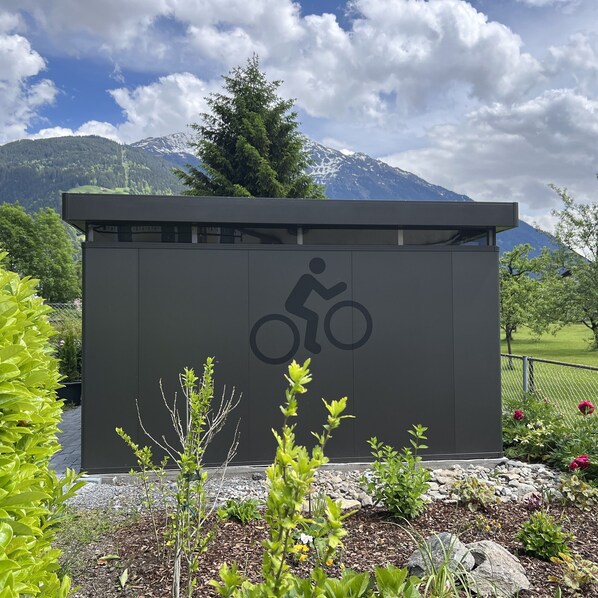 Un bâtiment moderne orné d’un symbole de vélo, entouré de verdure et avec des montagnes en arrière-plan.