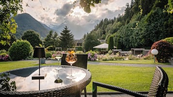 Ein Sitzbereich im Freien mit einem runden Tisch und Stühlen, einem Glas Weißwein und einem Cocktail mit Trinkhalm.