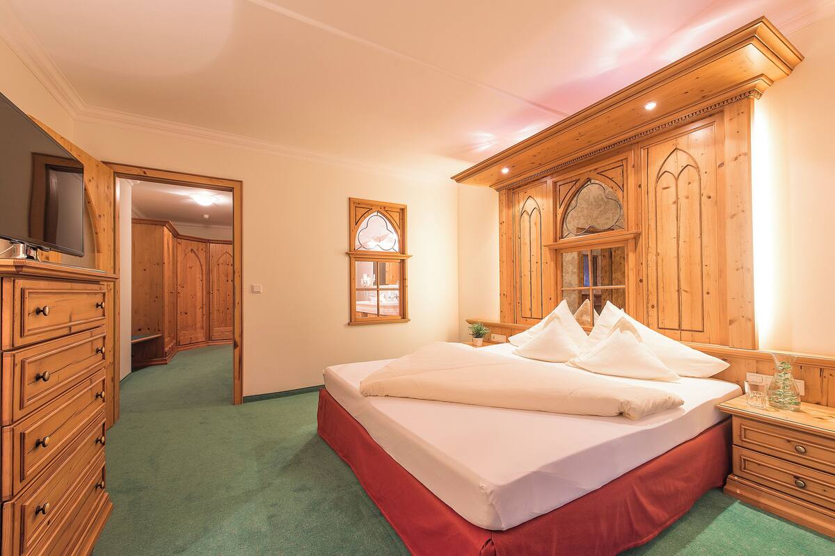 Un dormitorio con una cama grande, un armario de madera, un espejo y una mesita de noche con una lámpara.