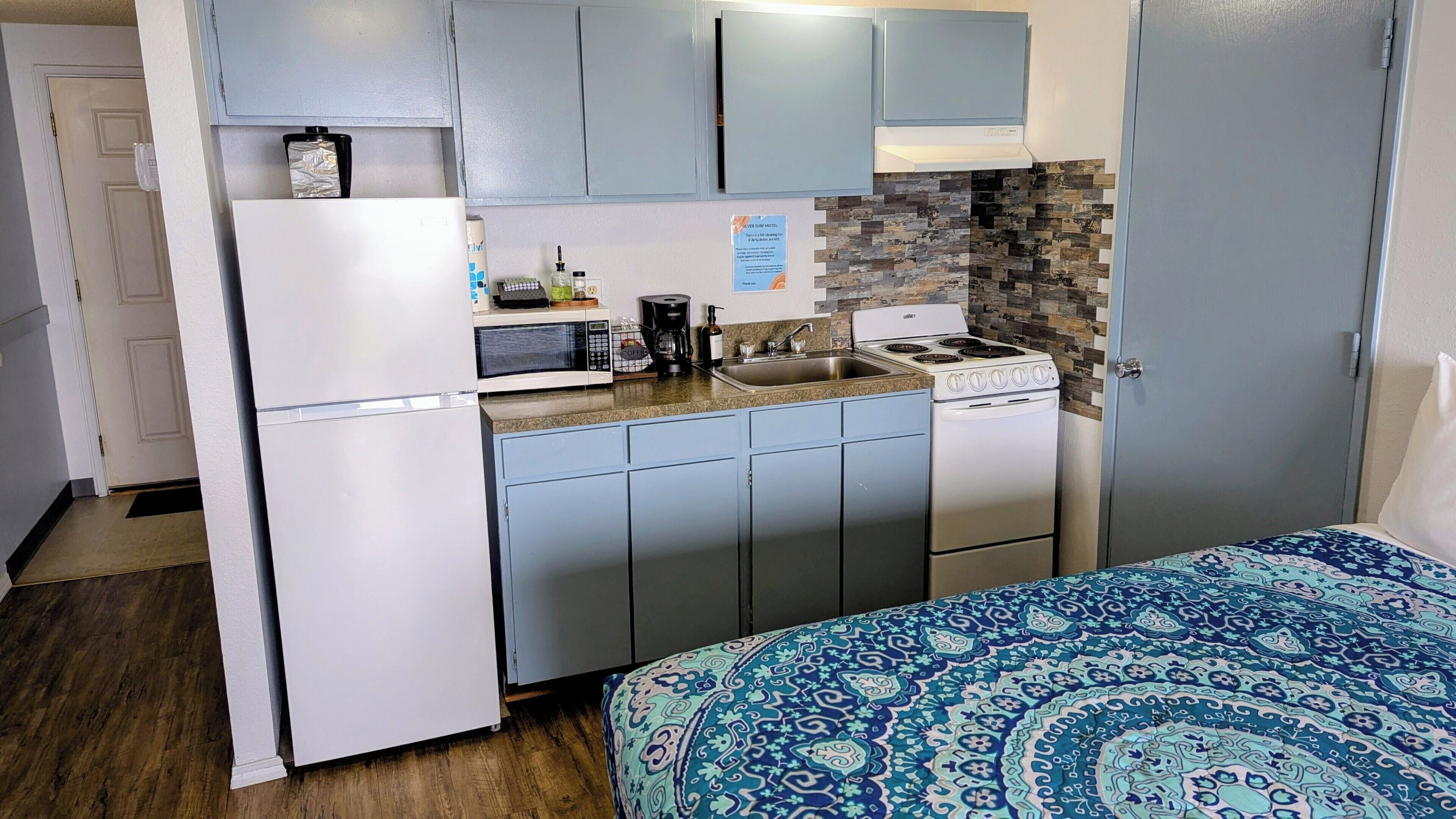 A compact kitchenette with a refrigerator, microwave, coffee maker, and stove.