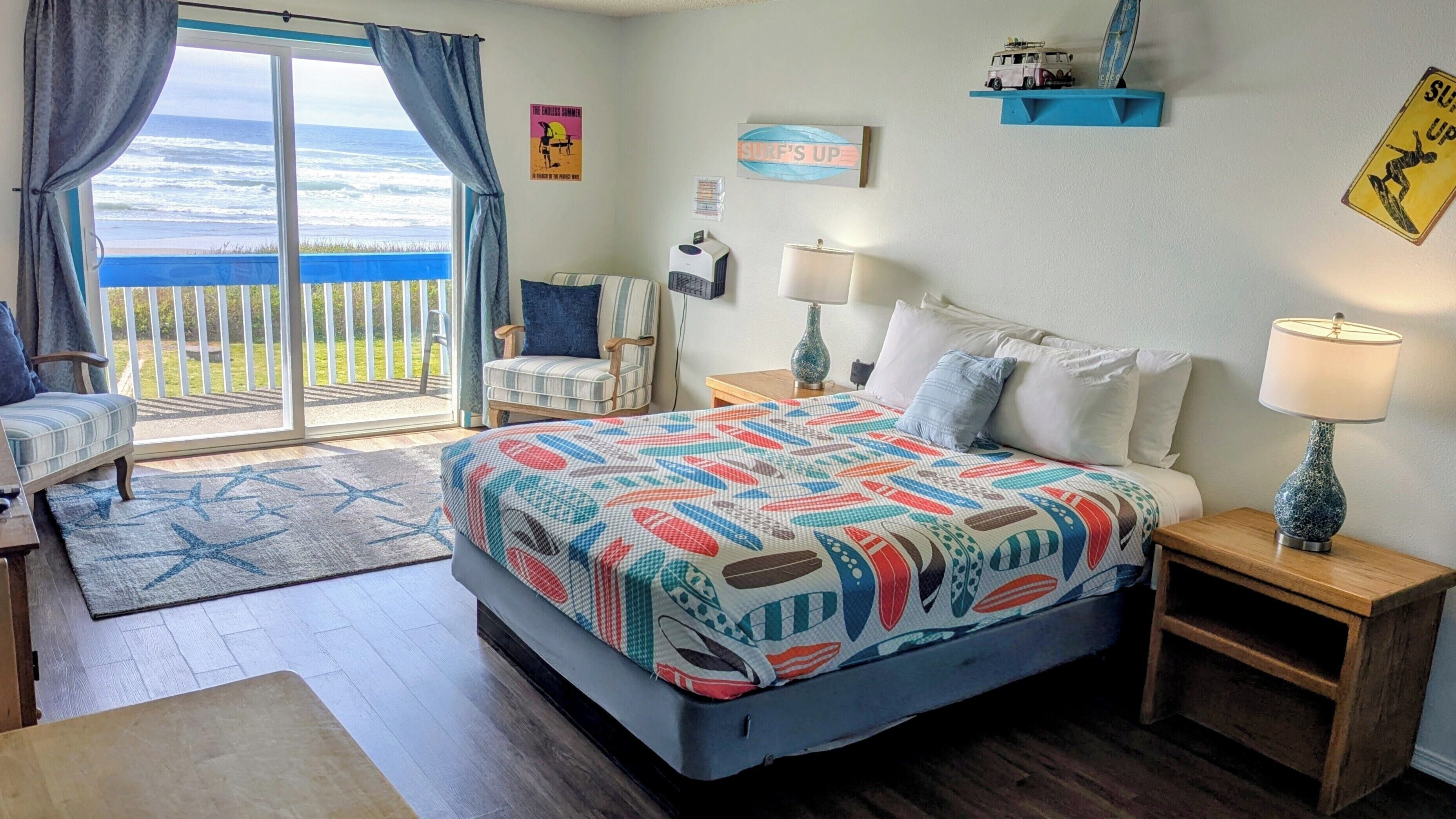 Un dormitorio con una cama grande, una silla, una mesita, una lámpara y vistas al océano.