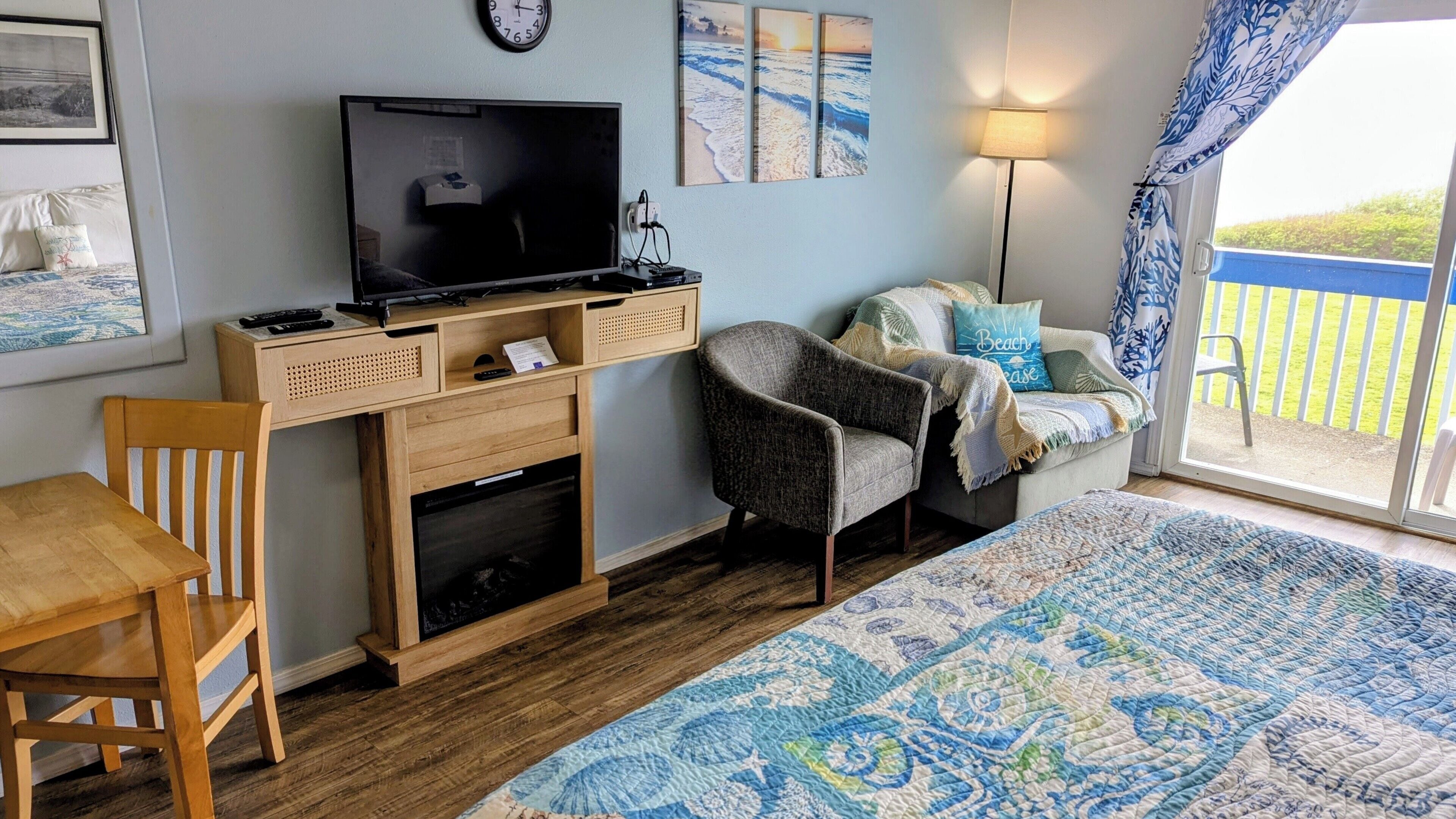 A room with a television, a desk, a chair, a sofa, a bed, a clock, and a view of the outdoors.