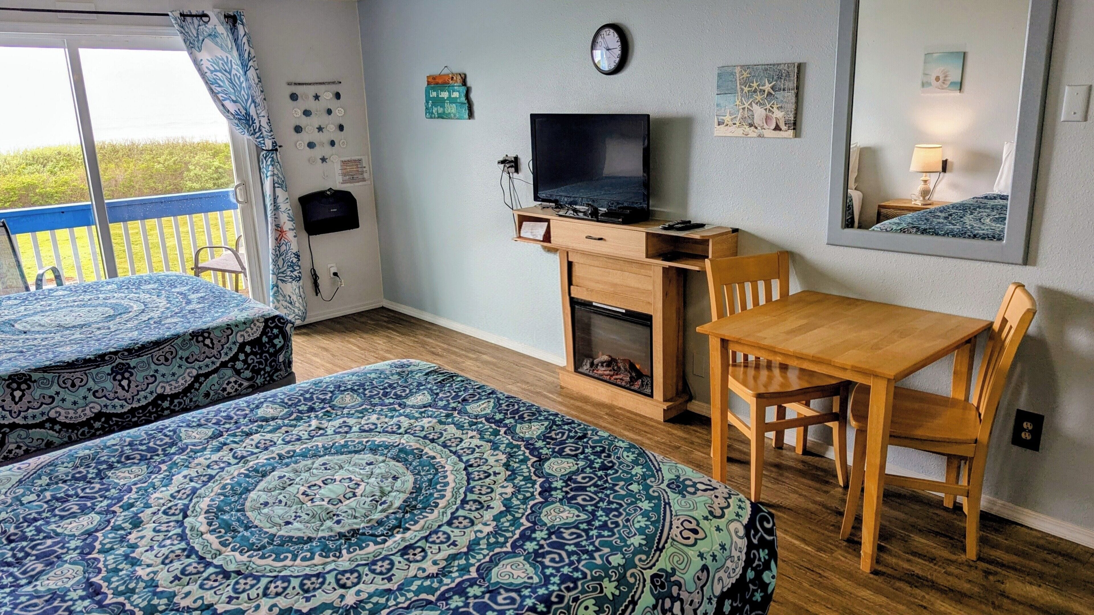 A room with two beds, a desk with a television, a fireplace, and a view of the outdoors.